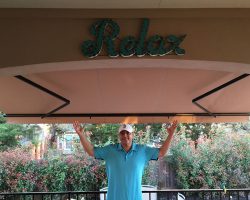 man in blue shirt holding his hands up under his beige awning that says "relax"